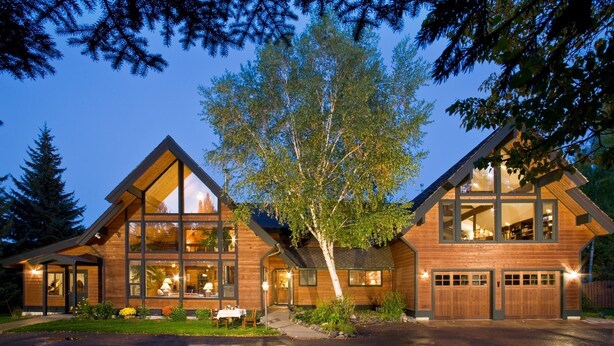 A modern log cabin with large windows, a covered patio, and a garage.