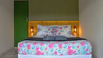 Un lit avec une literie à motifs floraux, une porte verte et deux lampes fixées au mur.