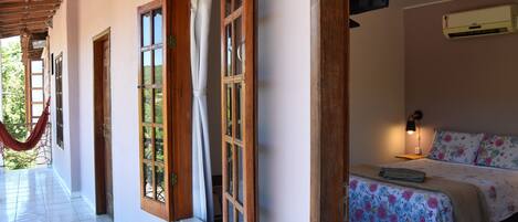 Una habitación con cama, ventana con cortinas, una hamaca afuera y un equipo de aire acondicionado.