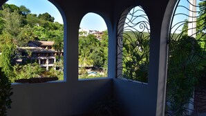A covered patio area with arched windows overlooking a lush garden and a pool.
