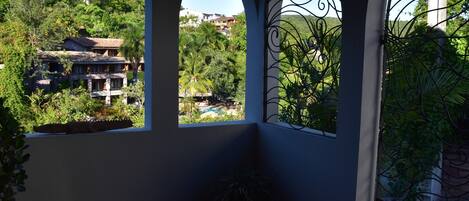 A covered patio area with arched windows overlooking a lush garden and a pool.