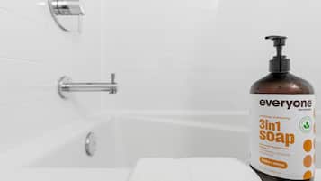 A bathroom with a white bathtub, a white towel, and a bottle of 3in1 Soap.