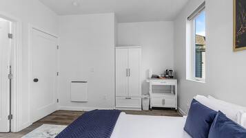 A bedroom with a bed, a wardrobe, a small desk with a chair, and a window.