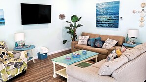 Un salon avec un canapé, des fauteuils, une table basse, un téléviseur et une plante.