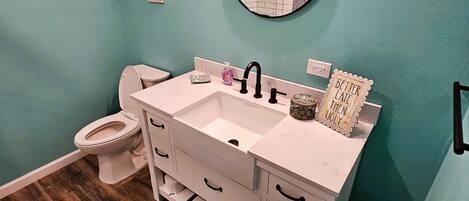 Une salle de bain avec un meuble-lavabo blanc, un miroir rond et des toilettes.
