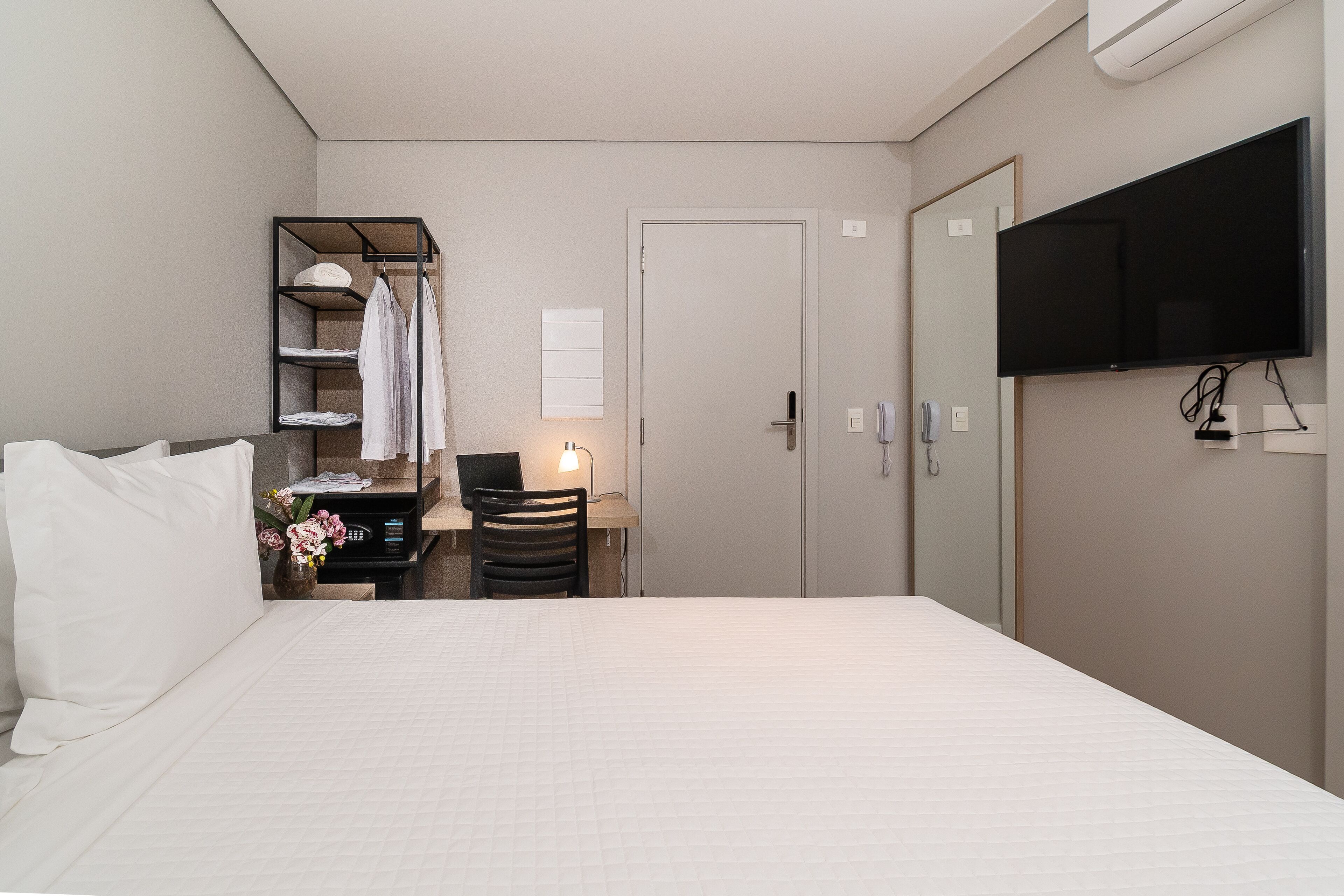 Une chambre d’hôtel comprenant un lit, un bureau avec une chaise, un téléviseur fixé au mur et une armoire.
