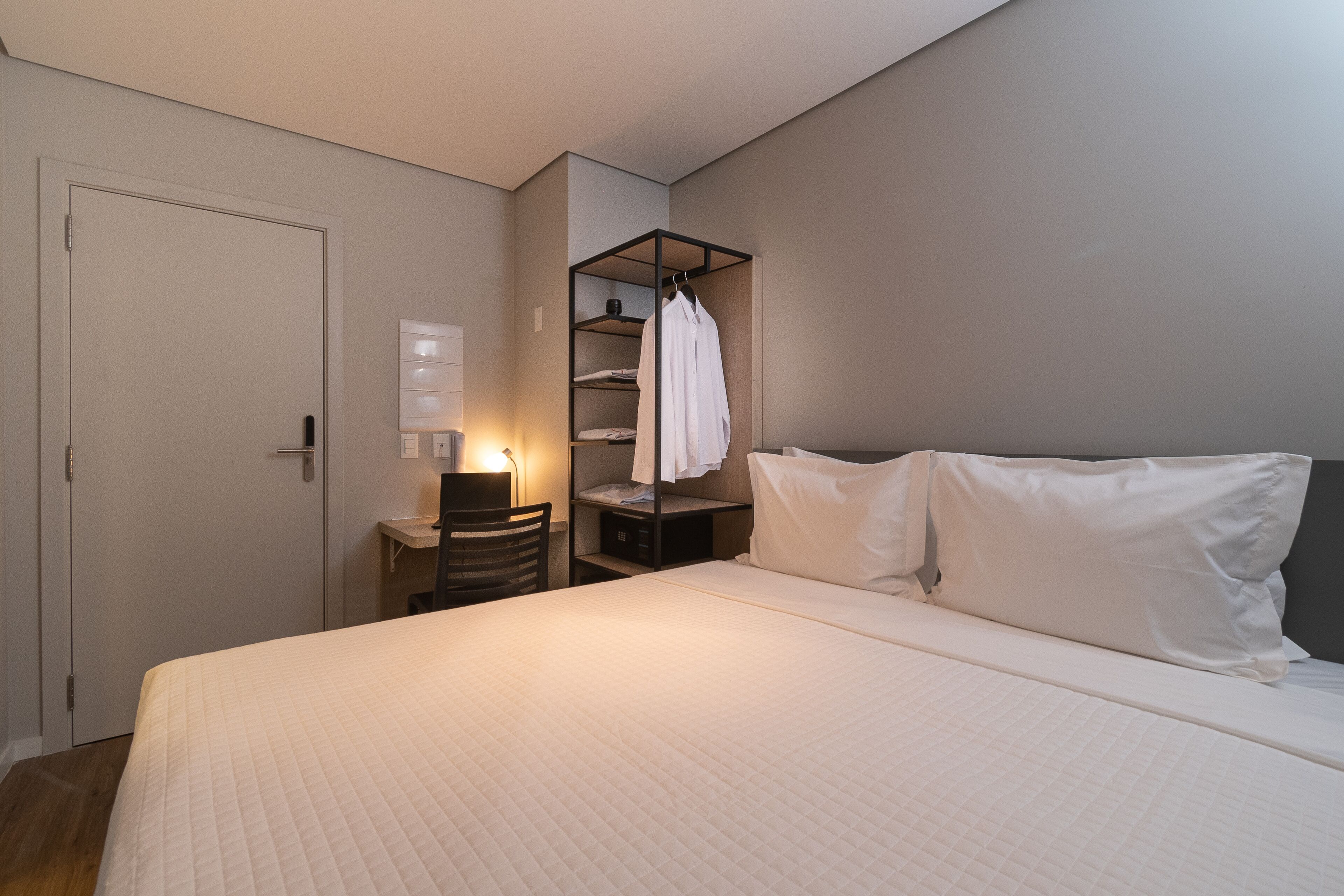 A bedroom with a bed, a bedside table, a chair, a wardrobe, and a shelf unit.