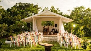 Une cérémonie de mariage en plein air, avec une tente blanche et des rangées de chaises blanches décorées de rubans colorés.