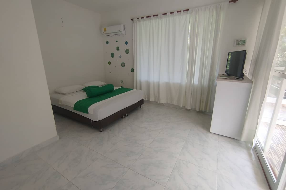 Habitació d'hotel amb un llit, una televisió sobre un suport i una finestra amb cortines.