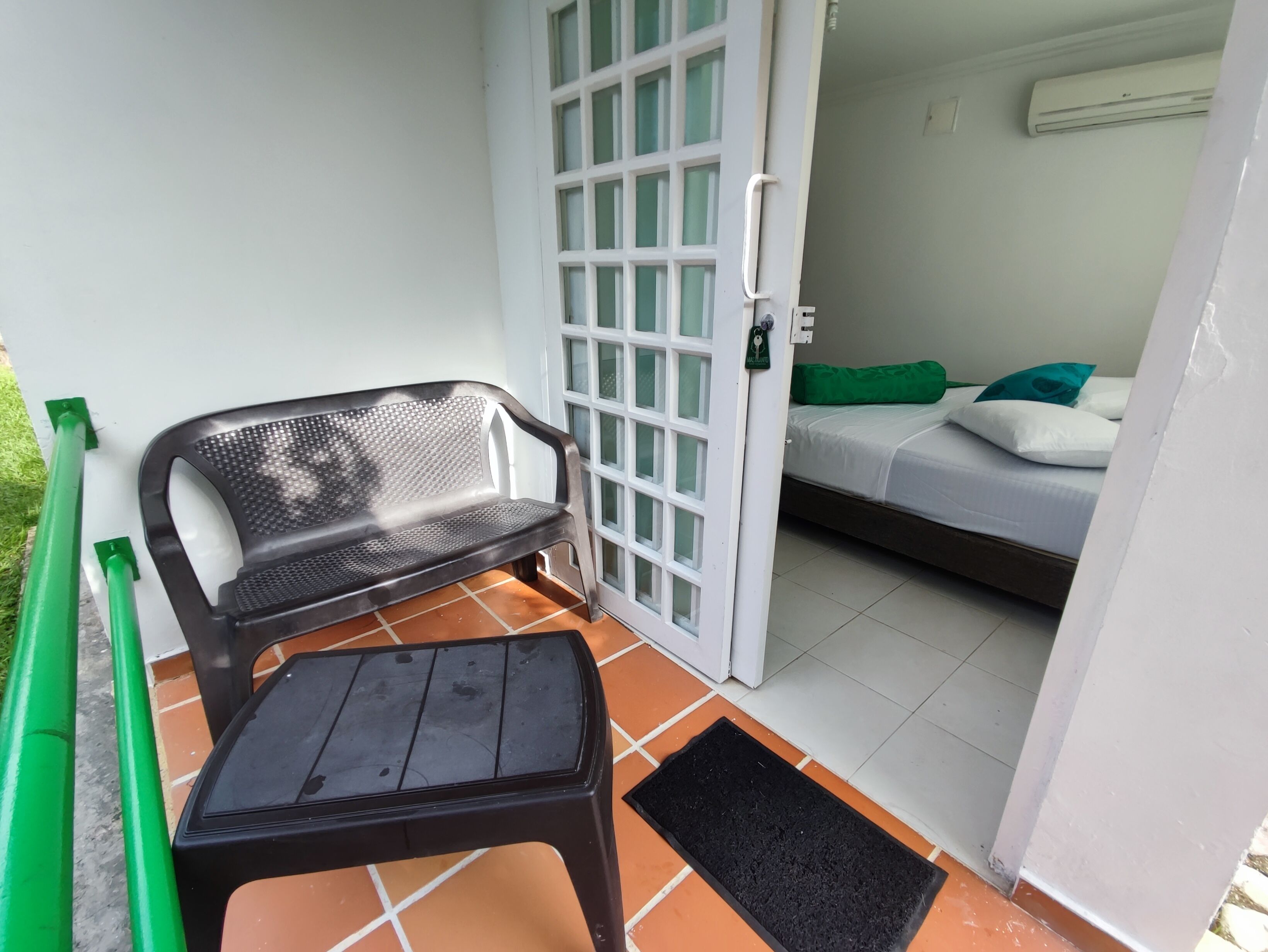 Una habitación con una cama, un banco, una puerta y una pequeña mesa.
