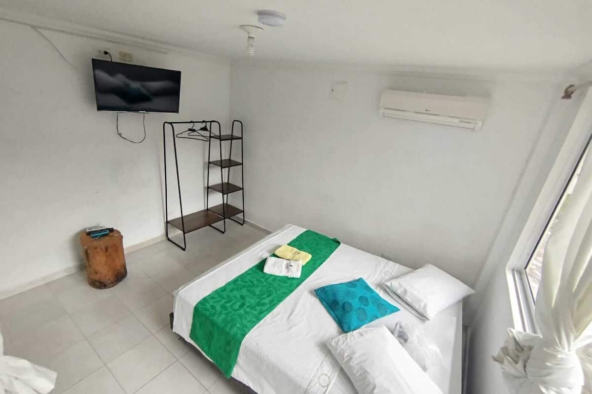 Habitació d'hotel amb un llit, televisió penjada a la paret, un tamboret de fusta i un aparell d'aire condicionat.