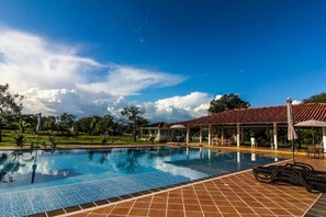 A swimming pool with tiled edges, a covered seating area with umbrellas, and a clear blue sky. - Hotel Campestre Mastranto (Villavicencio)