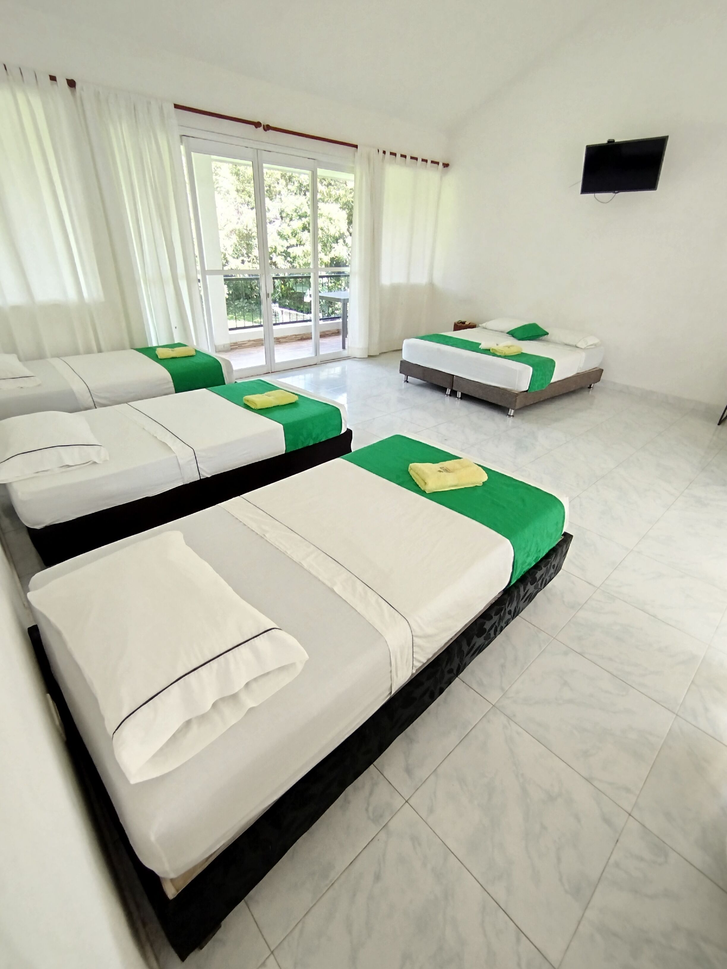 Habitación de hotel con cuatro camas, televisión y balcón con vista a zonas verdes.