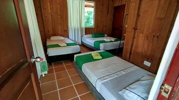 Una habitación de cabaña de madera con tres camas, cada una con ropa de cama verde y almohadas blancas.