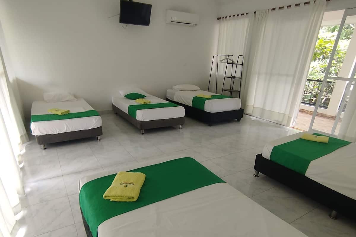Habitació d'hotel amb quatre llits, cada un amb roba de llit blanca i verda, televisió de pantalla plana, aire condicionat i un balcó amb vistes.