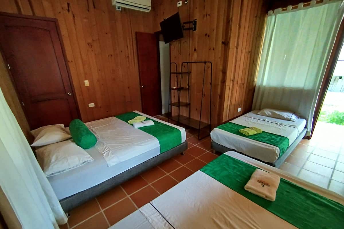 Habitació amb dos llits individuals, parets de fusta, una petita televisió i una finestra amb cortines.