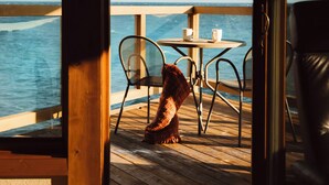 Une terrasse en bois avec une table et des chaises, donnant sur une étendue d’eau.