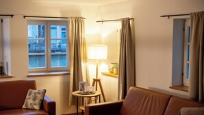 Un salon chaleureux avec un canapé en cuir marron, une petite table ronde avec une lampe et une fenêtre avec des rideaux.