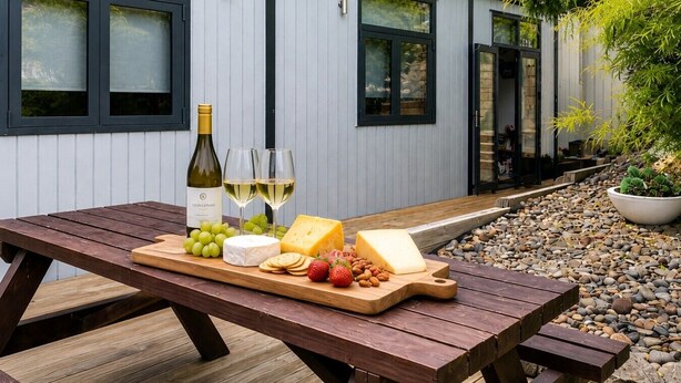 Ein Holztisch für ein Picknick, mit einer Weinflasche, Gläsern, Käse, Trauben, Erdbeeren und Mandeln.