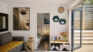 Ein modernes Interieur mit einem grauen Sofa, einem Holztisch, einem großen abstrakten Gemälde, einer sechseckigen Uhr und einer Glastür, die zu einem Außenbereich führt.