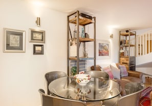 Uma sala de estar moderna com uma mesa de jantar de vidro, cadeiras de metal, um sofá e uma estante embutida.