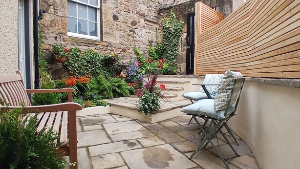 A stone courtyard with a wooden bench, a folding chair, and a small table.
