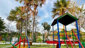 Un terrain de jeux avec des structures colorées, notamment des toboggans et des balançoires, entouré d’arbres et sous un ciel dégagé.