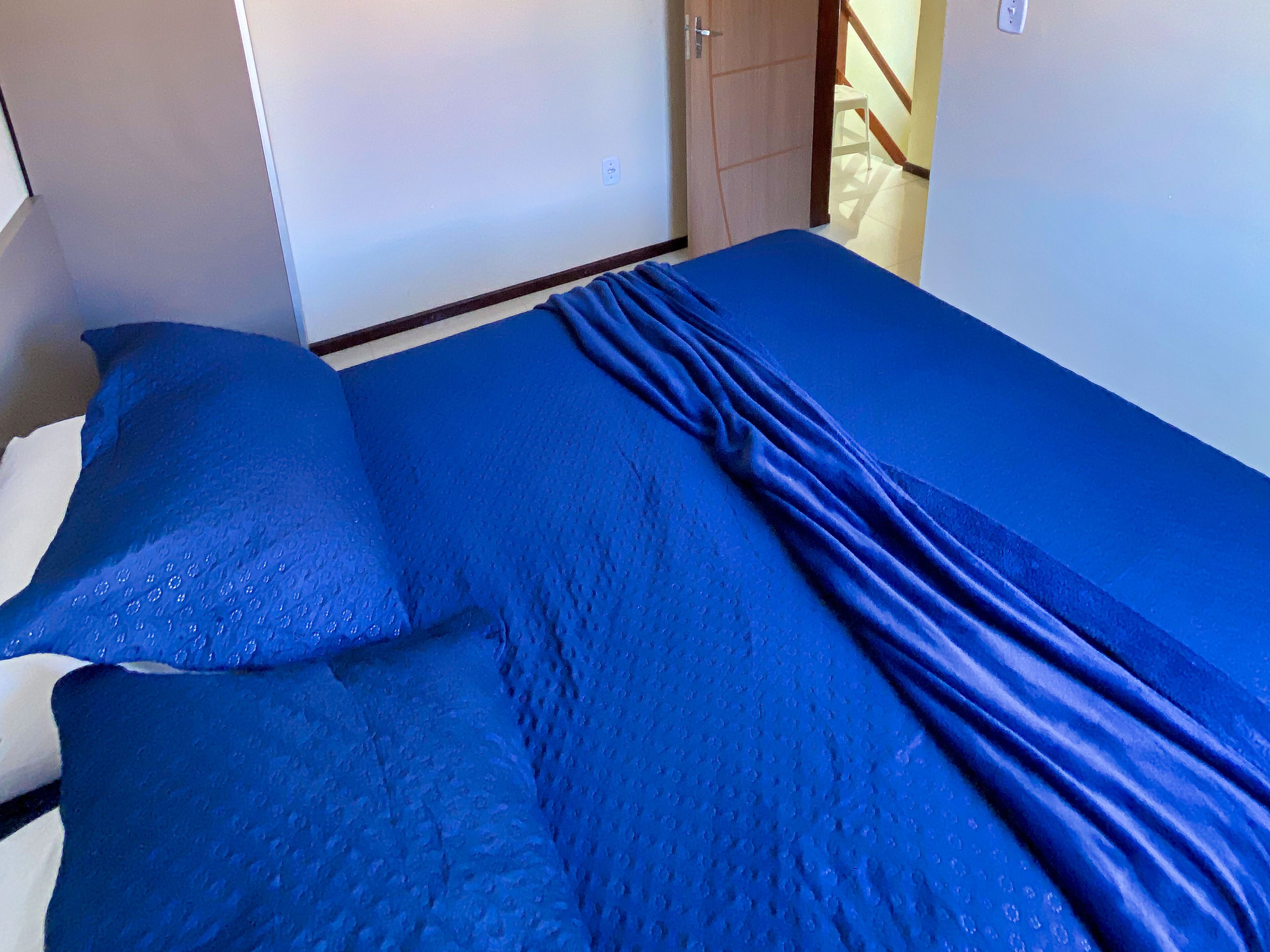 A room with a bed covered in blue bedding, a white wall, and a door.