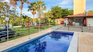 Une piscine dotée d’une terrasse carrelée, entourée de palmiers et d’une aire de jeux.