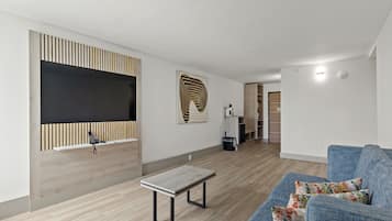 A modern living room with a sofa, a coffee table, a TV mounted on a wooden panel, and a patterned artwork on the wall.