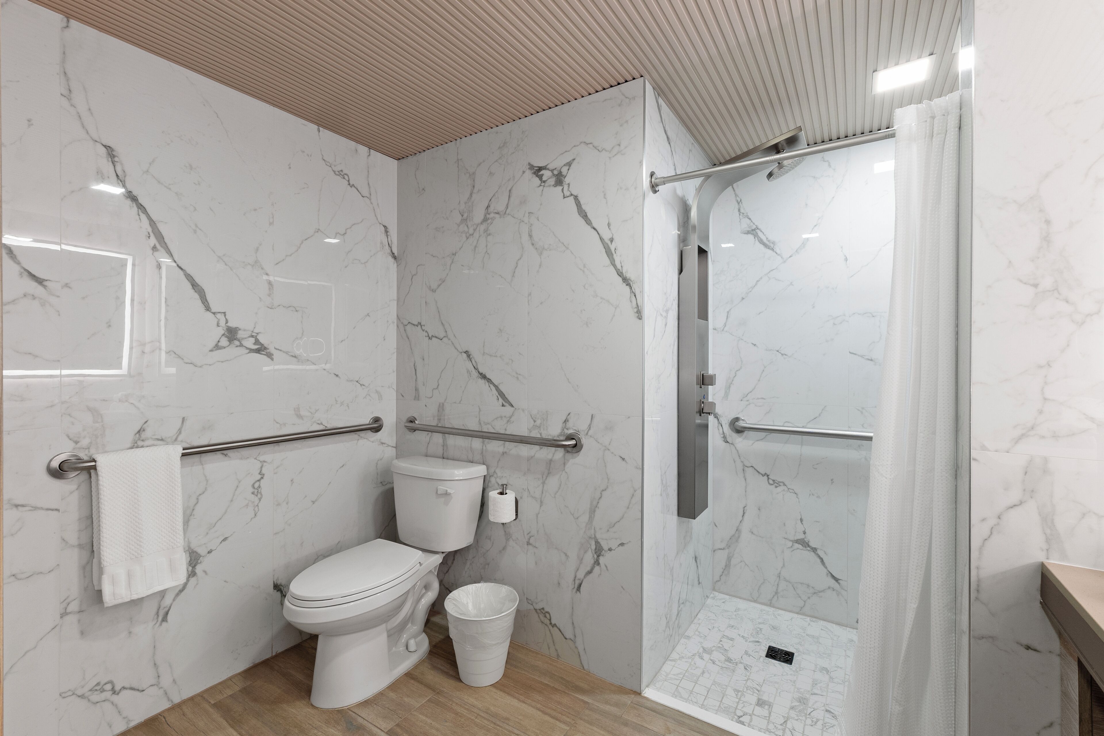 Un baño moderno con paredes de mármol, inodoro, ducha con puerta de vidrio y suelo de madera.
