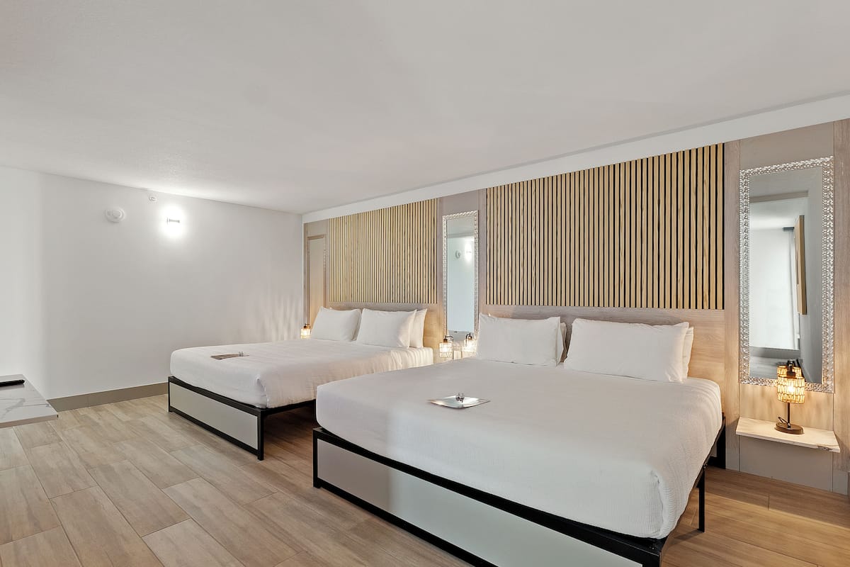 A hotel room with two beds, a wooden slat wall, a mirror, and a bedside table with a lamp.