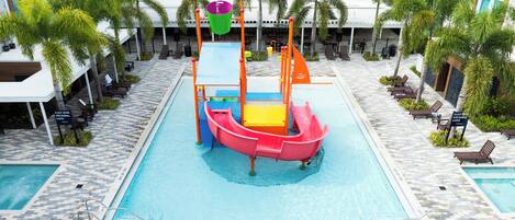 A pool area with a water slide, lounge chairs, and palm trees.