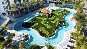 Área de piscina en un resort, con un diseño de piscina sinuosa, sillas de descanso y palmeras.