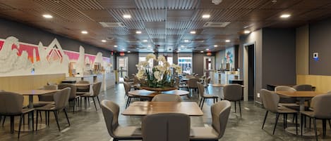 A modern restaurant with wooden ceiling panels, a central floral arrangement, and multiple dining tables and chairs.