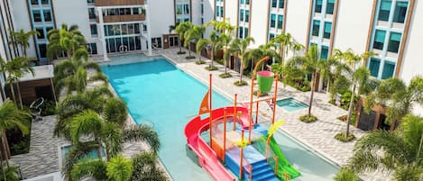 Ein modernes Hotel mit Pool, Palmen und einem Wasserspielplatz für Kinder.
