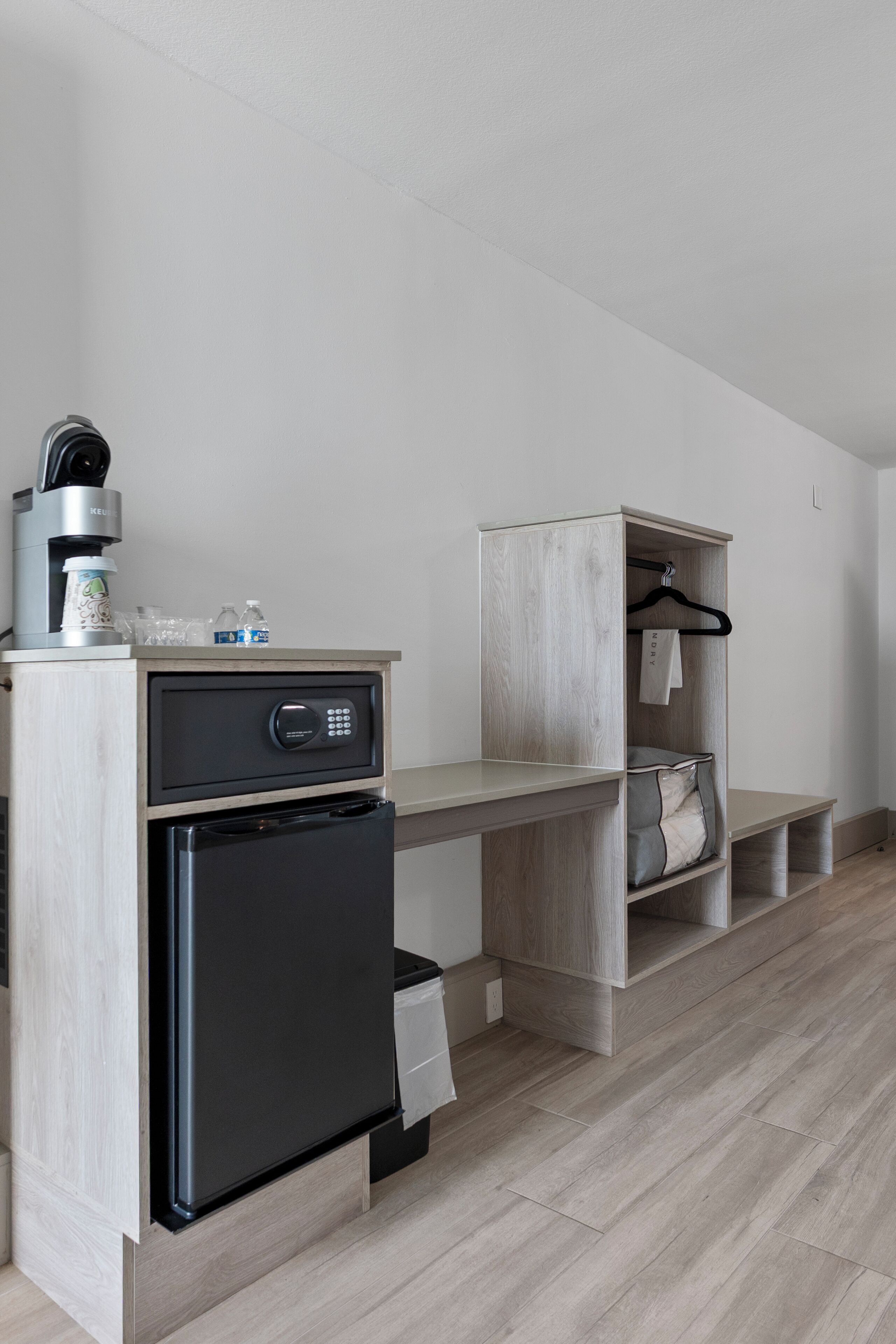 Une cuisine moderne et compacte, équipée d’une machine à café intégrée, d’un réfrigérateur et d’un meuble de rangement en bois doté d’étagères.