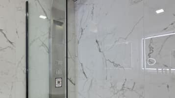 A modern bathroom with a glass-enclosed shower, marble walls, and a visible control panel.