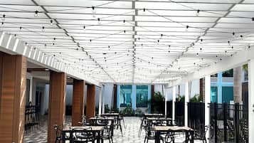 Un espace extérieur abrité, aménagé avec des tables et des chaises, doté d’un sol à motifs et illuminé par des guirlandes lumineuses suspendues au plafond.