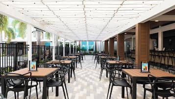 A spacious outdoor dining area with multiple tables and chairs, a patterned floor, and a ceiling with string lights.