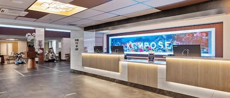 A modern reception area with a large digital display, a wooden reception desk, and a tiled floor.