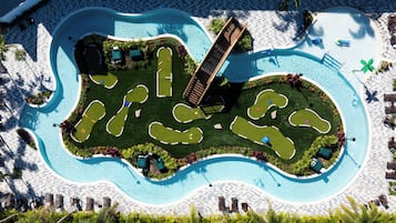 An aerial view of a resort with a large swimming pool, multiple lounge areas, and a well-maintained lawn.