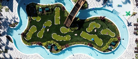 An aerial view of a resort with a large swimming pool, multiple lounge areas, and a well-maintained lawn.