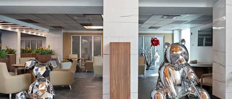A modern lobby with seating areas, a wooden column, and a large metallic sculpture.