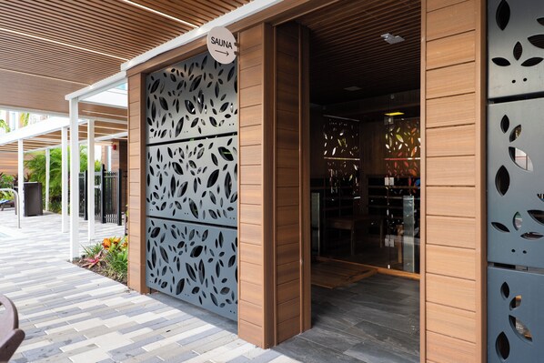 Entrada de un spa con fachada de madera, un letrero que indica una sauna y una partición de metal con diseño.