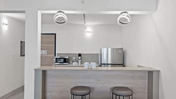 A modern kitchen with a central island, two bar stools, a microwave, a coffee maker, and a refrigerator.
