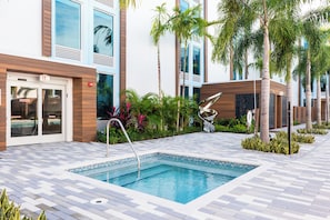 A swimming pool with a tiled deck, surrounded by palm trees and plants, and a building with a modern design. - Kompose Boutique Resort at Theme Parks (Kissimmee)