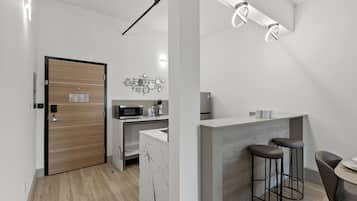 A modern kitchen with a microwave, coffee maker, and marble countertop. There is a wooden door and a bar area with stools.
