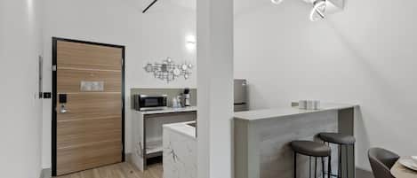 Eine moderne Küche mit Mikrowelle, Kaffeemaschine und Marmorarbeitsplatte. Eine Holztür und ein Barbereich mit Barhocker sind vorhanden.