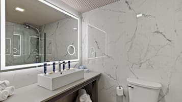 A modern bathroom with a marble backsplash, a large mirror with integrated lighting, a white sink with a vanity, and a toilet.